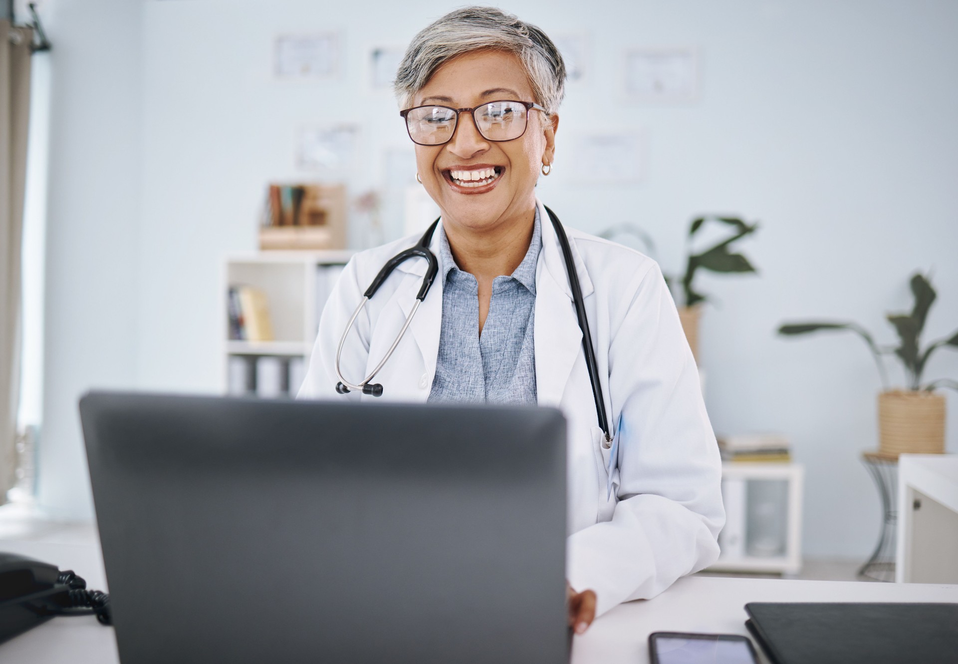 Woman doctor, laptop and happy in hospital office while working online for consultation or research. Medical professional female with internet for advice, healthcare and innovation or management